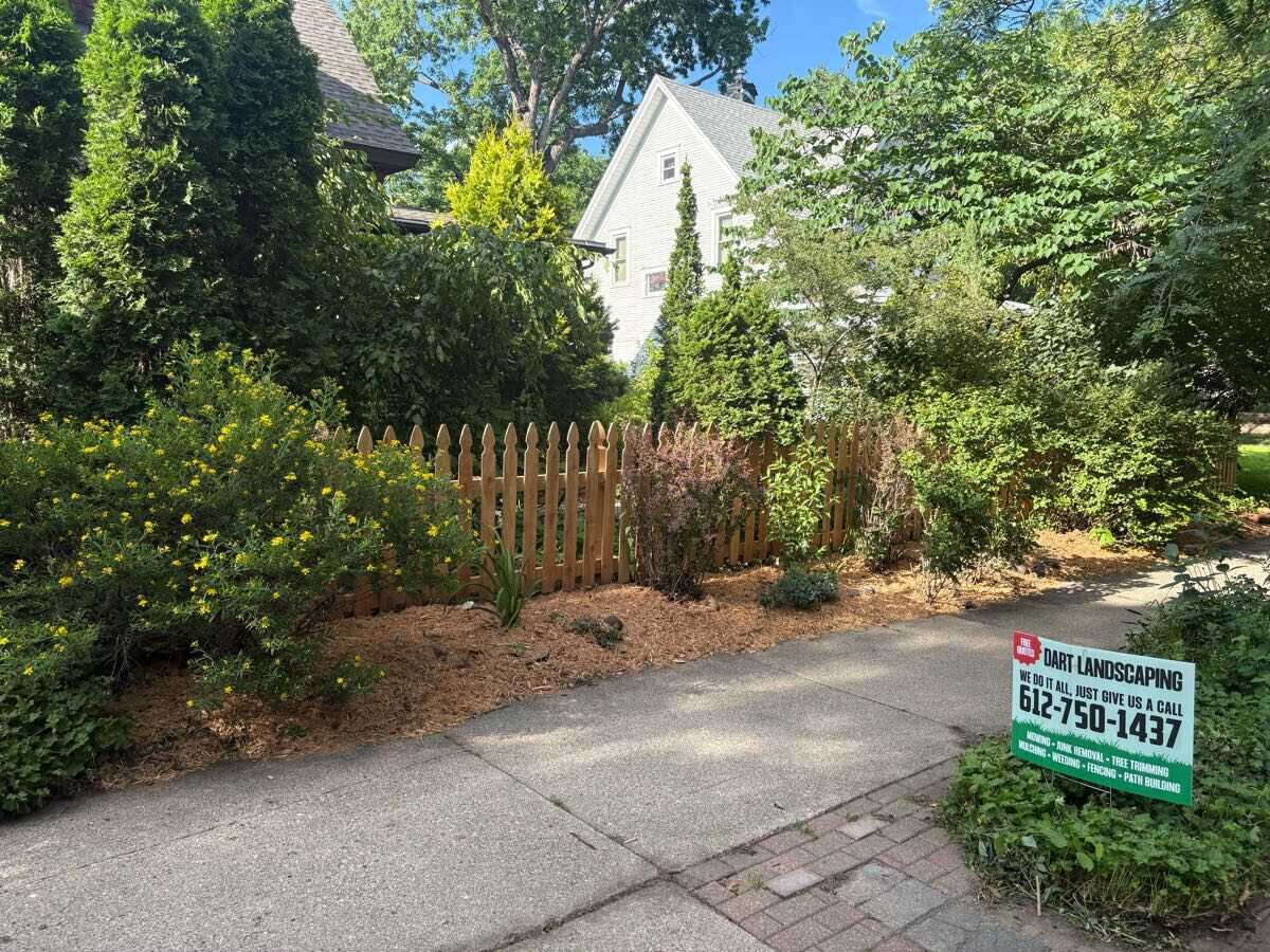 Freshly mulched garden beds along a new picket fence, with the Dart Landscaping yard sign